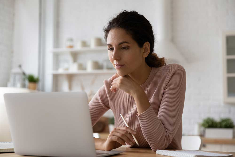 Woman works on a laptop computer while sitting in her living room