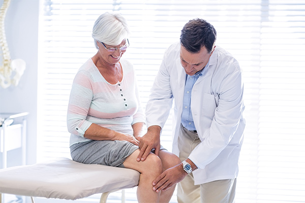 A doctor touches a woman's knee as she sits on a table.