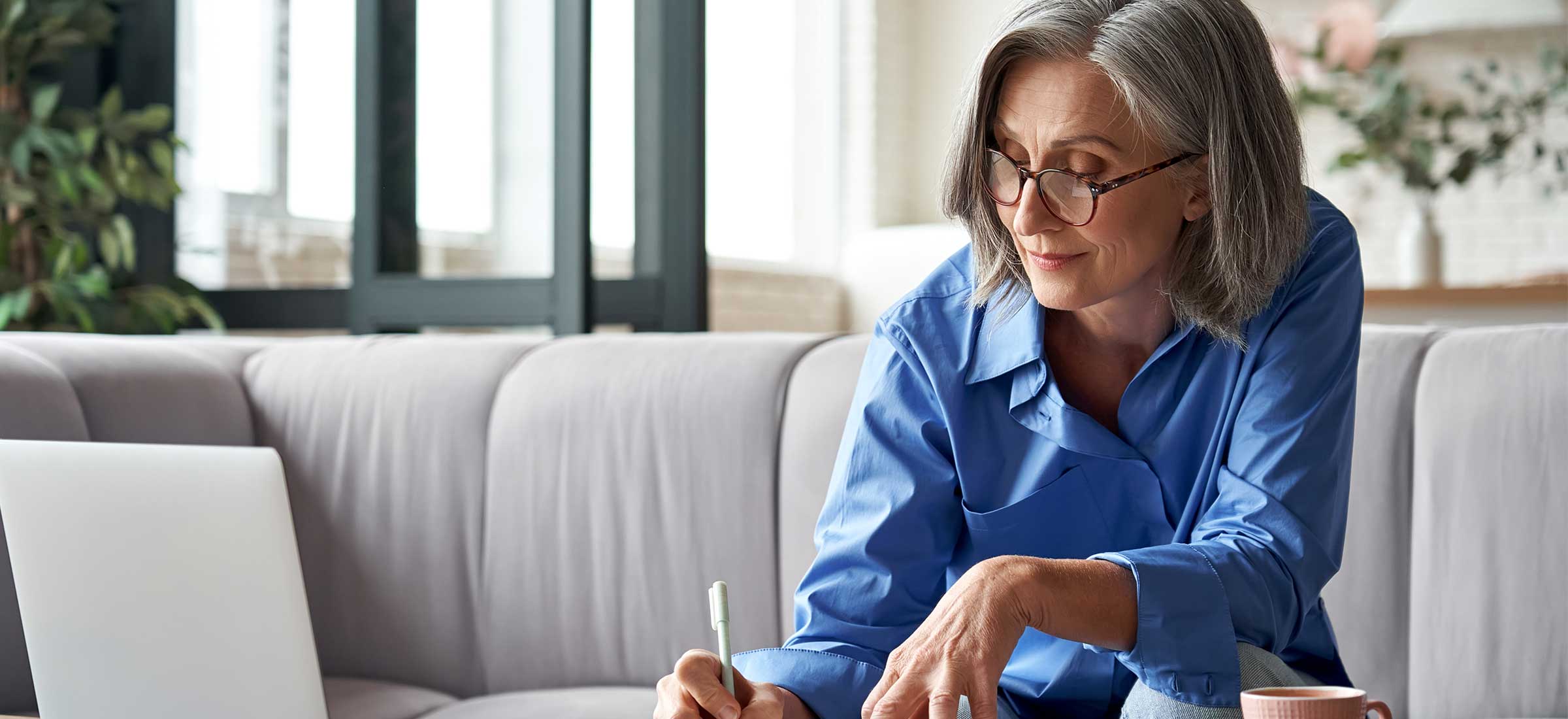 A woman sits on a couch and writes something.