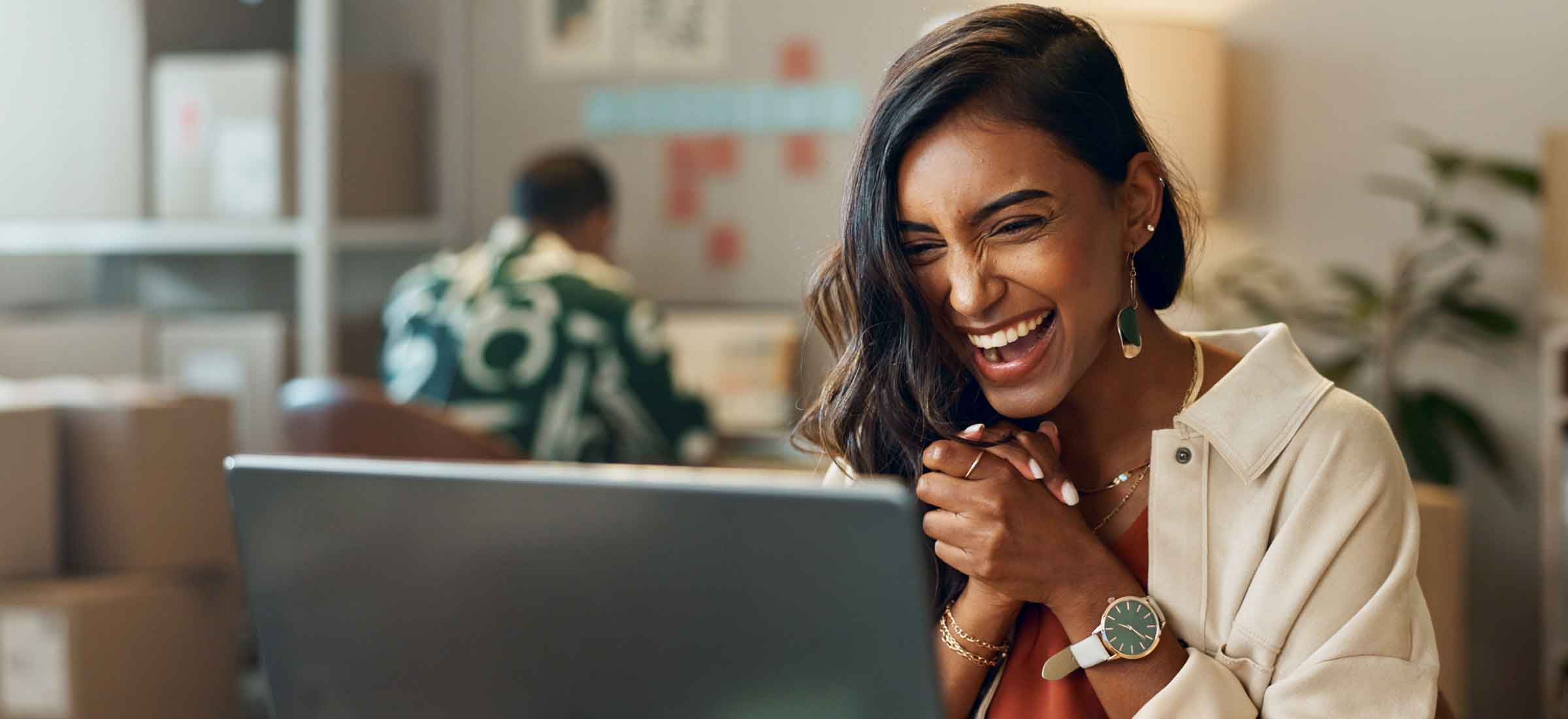 A woman claps her hands together and smiles while looking at a laptop.