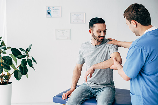 A doctor touches a patient's shoulder as he sits on a table in a medical office.