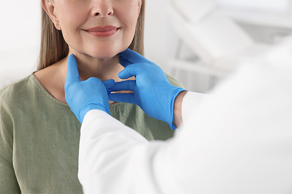 A doctor wearing blue gloves touches a woman's neck.