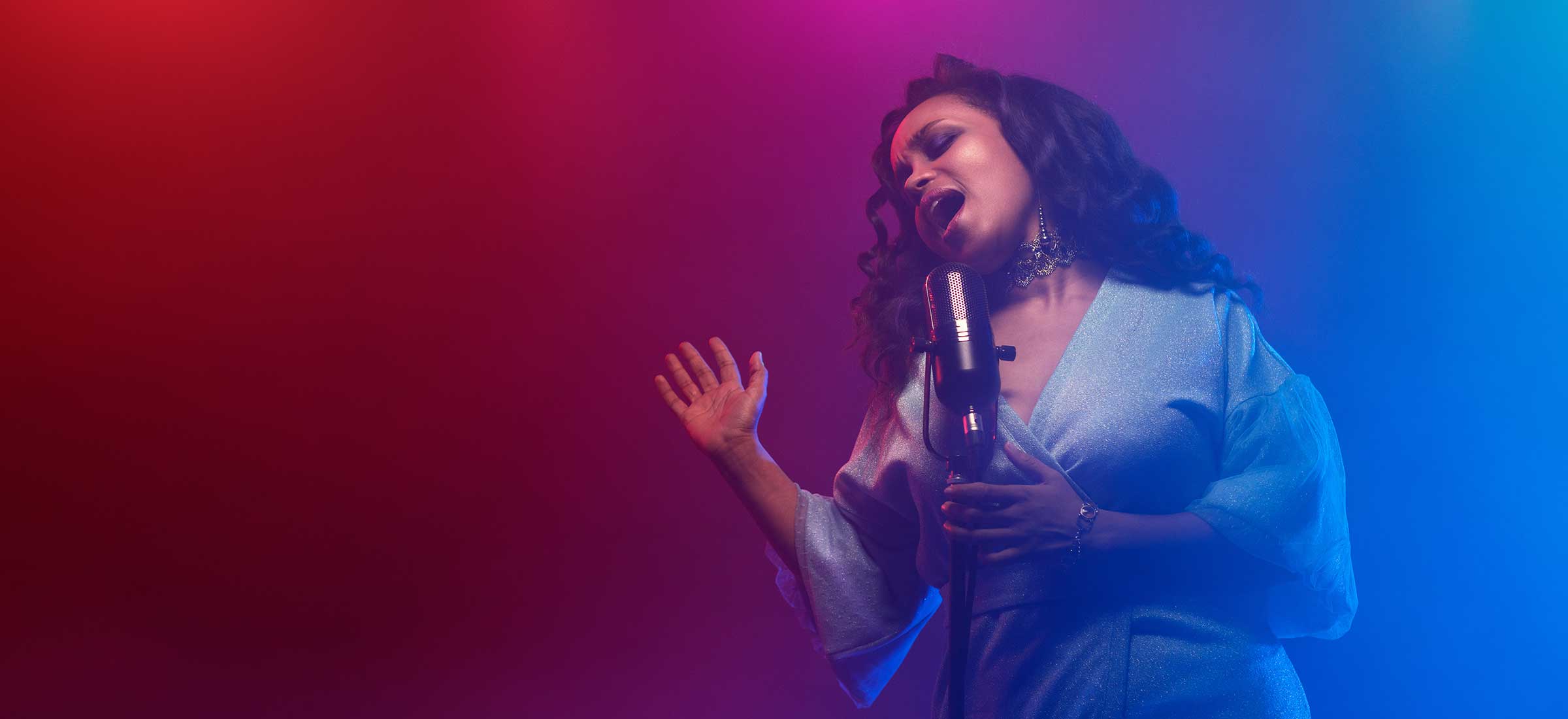 A woman sings into a microphone with a graphic background.