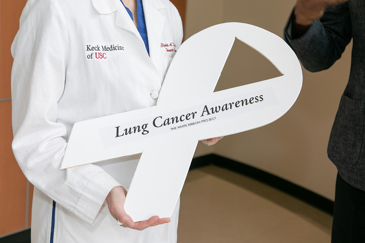 A Keck Medicine of USC oncology doctor holds a Chris Draft White Ribbon Project ribbon that reads Lung Cancer Awareness