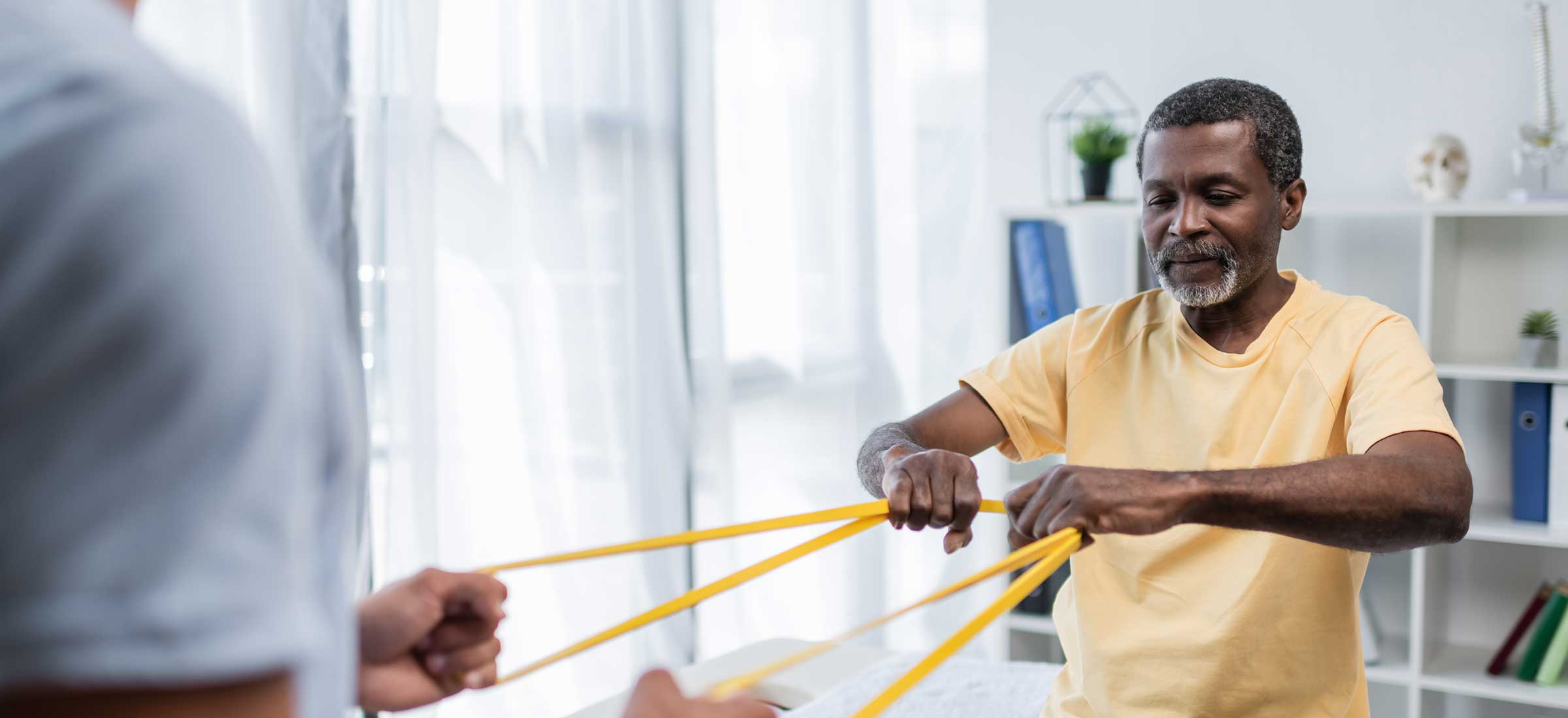 A senior man uses exercise bands at a physical therapy rehabilitation center