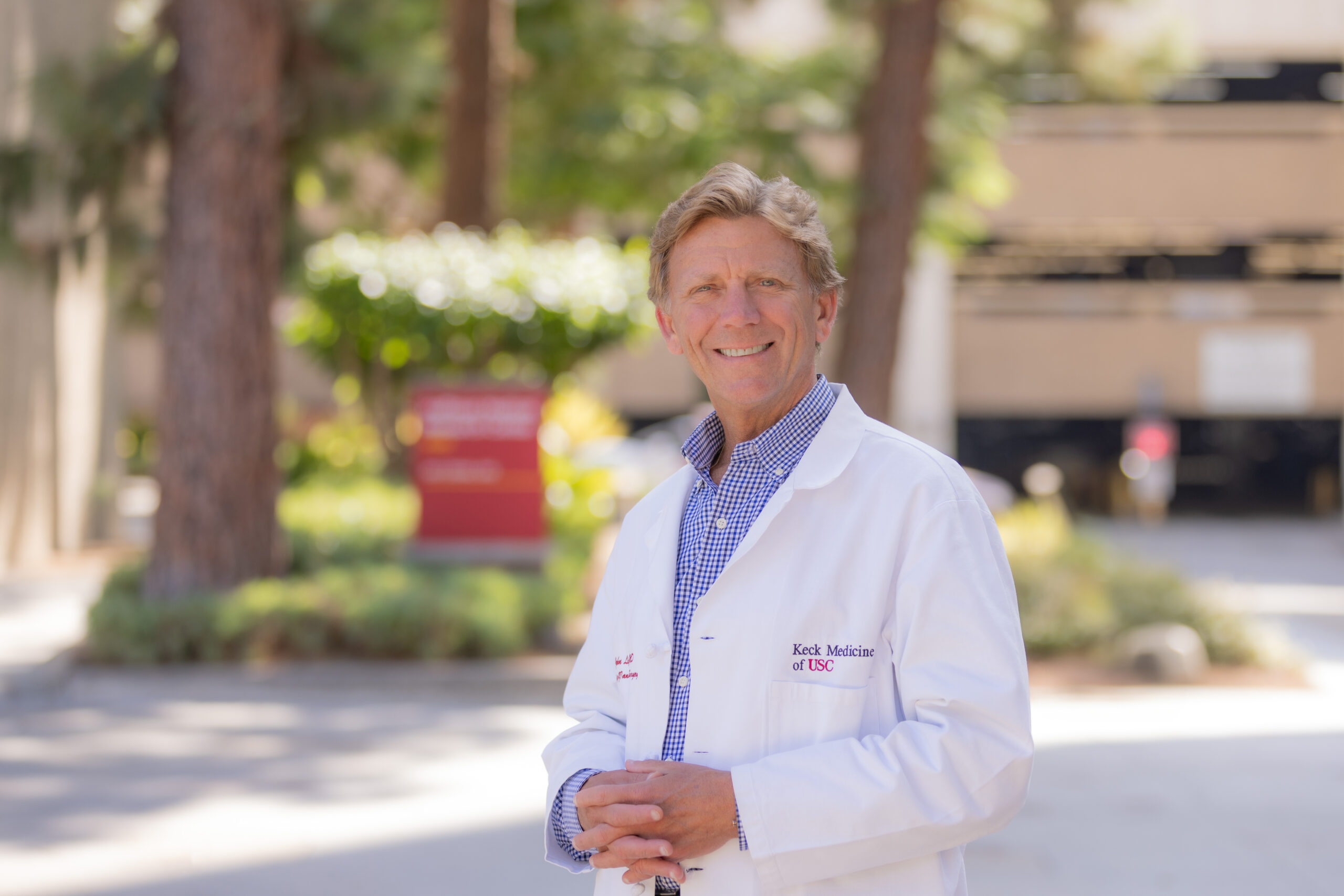 A portrait of Dr. John Lipham standing on the Keck Medicine of USC campus smiling in a white medical coat.