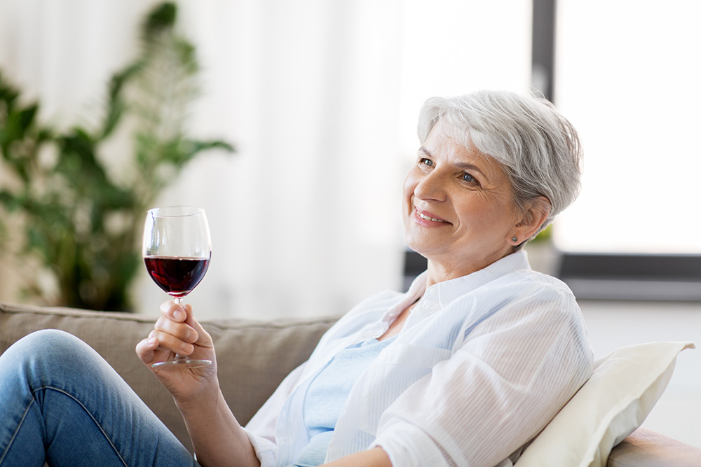 Senior woman enjoys drinking glass of red wine at home.