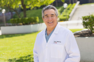 Dr. David Ginsberg stands outside in a white medical coat and smiles.