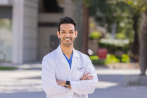 Dr. Junaid A. Zaman stands outside in a white coat and smiles.