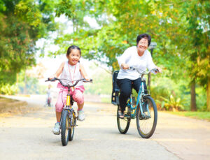A grandmother and granddaughter riding bikes through the park together